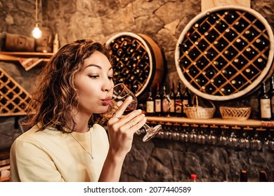 An Asian Woman Tastes And Analyzes Wine In The Cellar Of A Local Winery. Concept Of Tours And Sommelier Work