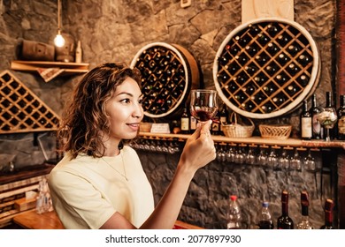 An Asian Woman Tastes And Analyzes Wine In The Cellar Of A Local Winery. Concept Of Tours And Sommelier Work