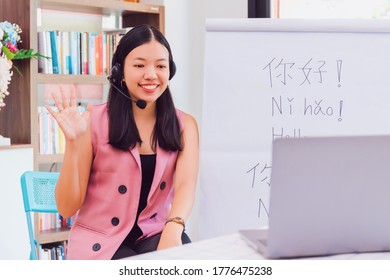 Asian woman teacher teaching remotely at home office with online technology laptop.Teaching Chinese language for Students at home school.Translation on paper text "Hello-How are you?"