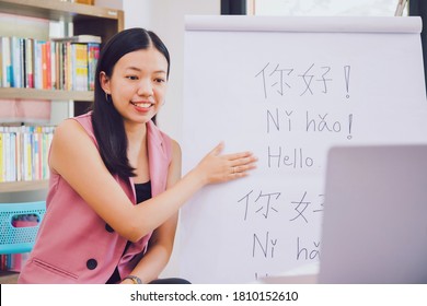 Asian woman teacher teaching remotely at home office with online technology laptop.Teaching Chinese language for Students at home school.Translation on paper text "Hello-How are you?"
