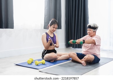 Asian Woman Teaching Her Mother Elderly Woman To Lift Dumbbells, Watching Video On Tablet, Home Healthcare Concept.