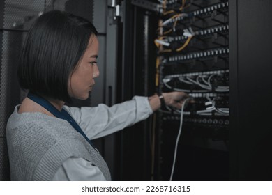 Asian woman, technician and server room for cabling, networking or system maintenance at office. Female engineer plugging wire for cable service, power or data security in admin or network management - Powered by Shutterstock