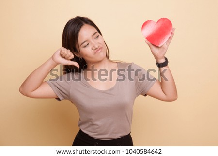 Asian woman thumbs down with red heart on beige background
