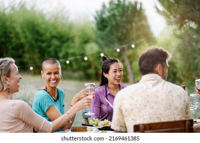 Asian Woman Together With Friends Having Dinner In A Garden On A Summer Evening, Drinking Wine, Having Fun And Laughing