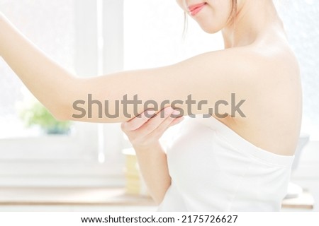 Asian woman touching her upper arm at home