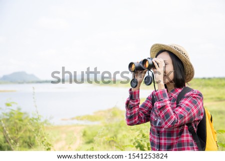 Asian woman tourist looking through binoculars in forest.