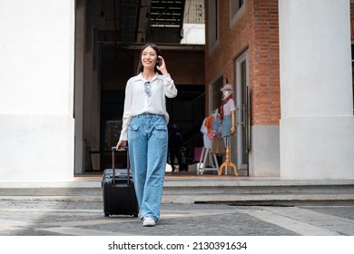 Asian Woman Tourist Talking On Smartphone While Walking To Dragging With Black Luggage To Passengers Lounge In The Airport For Holiday Trip