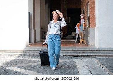 Asian Woman Tourist Is Traveling On Holiday Trip With Hat And Dragging Her Black Luggage While Walking To Passengers Lounge In The Airport