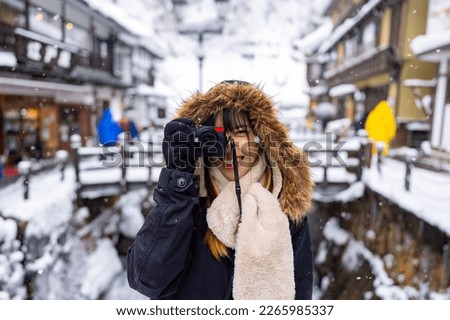 Asian woman tourist using digital camera taking picture during travel Ginzan onsen area in Yamagata prefecture, Japan in snow day. Attractive girl travel local village landmark on winter vacation.