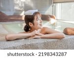 Asian woman with towel on head resting by the hotspring pool looking on right