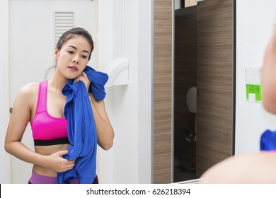 Asian Woman Toweling Her Face And Looking On Reflection In The Mirror After Exercise In Gym Dressing Room.