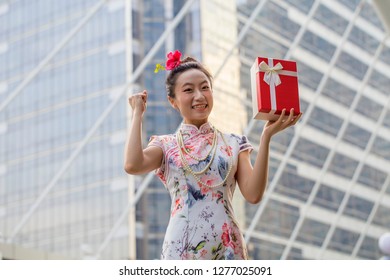 Asian woman in traditional chinese long dress, cheongsam, black hair, give a present and surprised get gift box for reward as a customer for Chinese New Year festival, celebration time.