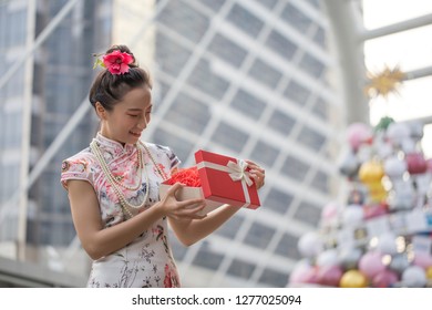 Asian woman in traditional chinese long dress, cheongsam, black hair, give a present and surprised get gift box for reward as a customer for Chinese New Year festival, celebration time.