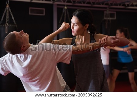 Asian woman training elbow strike with caucasian man in gym during self-defence training.