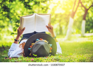 Asian Woman Travel Nature. Travel Relax. Sleep Reading Book On The Lawn In The Park. In Summer.