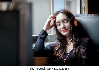 Asian woman traveler has listening music with phone and orange headphone inside the train at Hua Lamphong station at Bangkok, Thailand. - Powered by Shutterstock