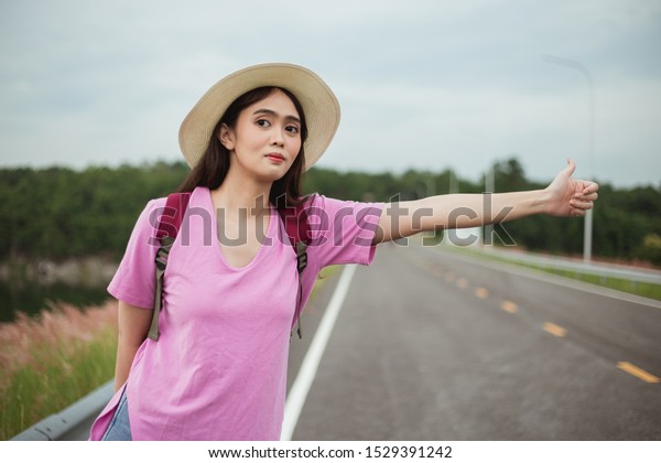 Asian woman traveler with hat and\
backpack wait call a car in summer. Traveler alone\
concept.
