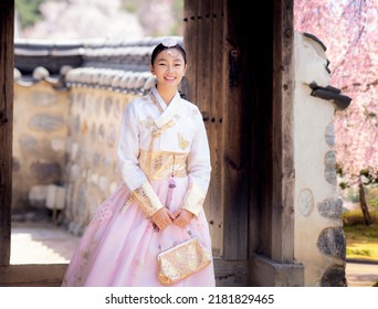 Asian Woman Traveler In Traditional Korean Dress Or Hanbok Dress Walking In Old Palace With Sakura Flower Background, Seoul City, South Korea