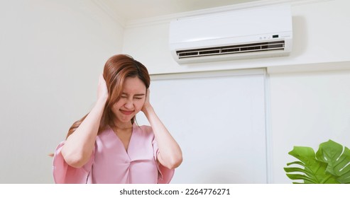 asian woman trying covering her ears is annoyed and she is suffering noise from air conditioner at home