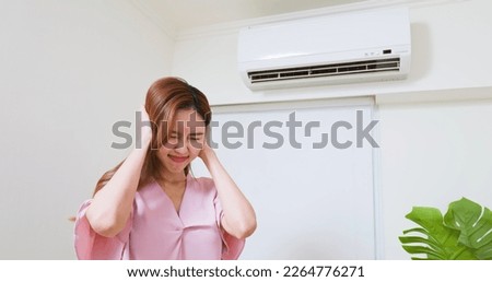 asian woman trying covering her ears is annoyed and she is suffering noise from air conditioner at home