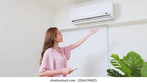 asian woman is turning on air conditioner through switching remote controller at home - Shutterstock ID 2266194825