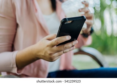 Asian Woman typing text message on smart phone in a cafe. Cropped image of young woman sitting at a chair with a coffee using mobile phone.