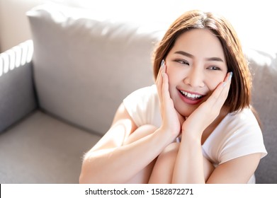 Asian Woman Use Her Both Hand Touch Her Face With Big Smile And Beaming Face In Her Liveingroom.