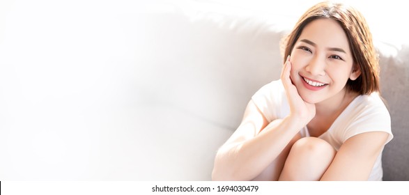 Asian Woman Use Her Both Hand Touch Her Face With Big Smile And Beaming Face In Her Liveingroom.