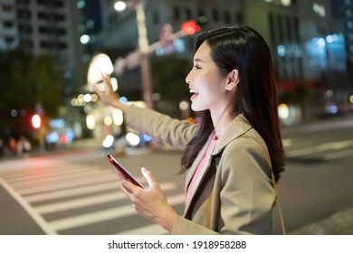 Asian Woman Use Smart Phone And Hail A Taxi On Road To Commute In The City At Night