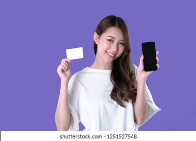 Asian woman use smartphone to payment online shopping with a blank credit card, white t-shirt clothing, purple background