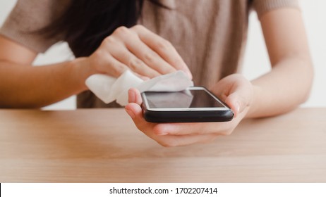 Asian Woman Using Alcohol Spray On Tissue Clean Mobile Phone Before Use It For Protect Coronavirus. Female Clean Surface For Hygiene When Social Distancing Stay At Home And Self Quarantine Time.