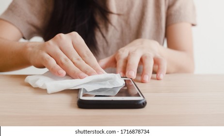 Asian Woman Using Alcohol Spray On Tissue Clean Mobile Phone Before Use It For Protect Coronavirus. Female Clean Surface For Hygiene When Social Distancing Stay At Home And Self Quarantine Time.