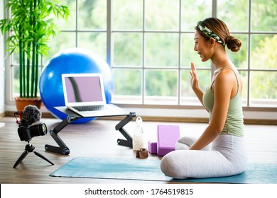 Asian woman using DSLR camera for live streaming teach yoga online in living room. Thai people smile work tutorial pratice to class room online for stray at home. - Powered by Shutterstock