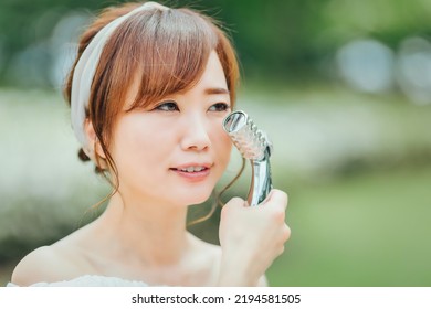 Asian Woman Using Facial Roller In Green