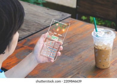 Asian Woman Using Futuristic Transparent Smartphone To Checking Cryptocurrency Online Trading And Analyzing Financial Data Stock Market At Coffee Shop