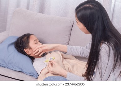 Asian woman using hands and thermometer to check high-temperature girl sickness headache, mother watch children lying down on sofa while mom worried daughter get fever illness, medical healthcare - Powered by Shutterstock