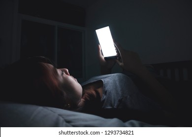 Asian Woman Using Her Mobile Phone On The Bed In Dark Room.