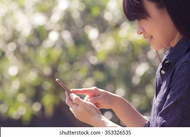 Asian Woman Using Her Mobile Phone In The Garden