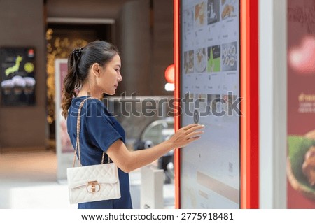 Asian woman using an interactive touchscreen kiosk to browse information in a modern shopping mall interior