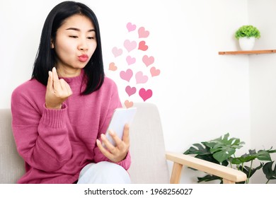 Asian woman using mobile phone dating online making hand sign mini heart flirting with her distance lover 