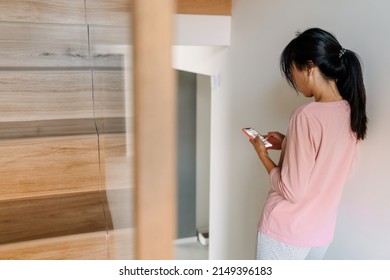 Asian Woman Using Mobile Phone While Going Up Stairs At Home