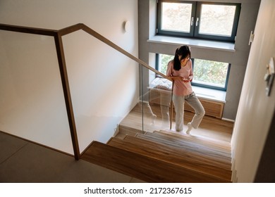 Asian Woman Using Mobile Phone While Going Up Stairs At Home