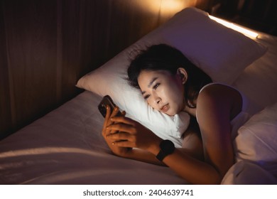 Asian woman using mobile phone smartphone laying on the bed in the bedroom. Sleepy exhausted, can not sleep. Insomnia, addiction concept. Women scrolling social networks on mobile dark bedroom. - Powered by Shutterstock