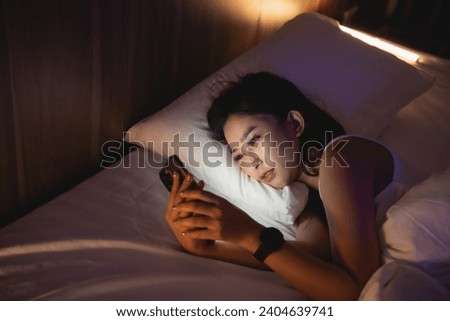 Asian woman using mobile phone smartphone laying on the bed in the bedroom. Sleepy exhausted, can not sleep. Insomnia, addiction concept. Women scrolling social networks on mobile dark bedroom.