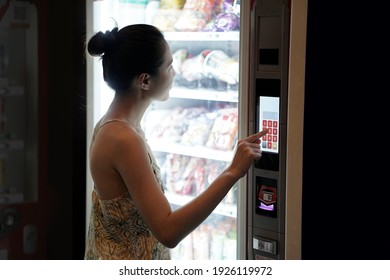Asian woman using a modern snack vending machine. Her hand touching on vending machine touch screen. Modern vending machine.