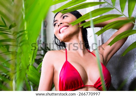 Asian woman using the shower in tropical garden before going to the swimming pool