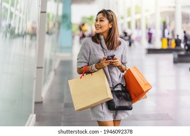 Asian woman using the smart mobile phone for check online shopping order with clothes beside the glassess in store shop at department center,shopaholic and fashion concept