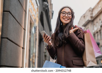 Asian woman using smartphone and looking away while enjoying a day shopping. Black friday, sale and discount. Buying clothes presents for holidays