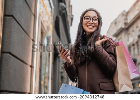 Asian woman using smartphone and looking away while enjoying a day shopping. Black friday, sale and discount. Buying clothes presents for holidays