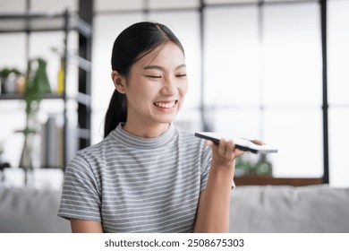 Asian woman using voice assistant on smartphone at home conversation with online assistant Voice chat bot conversational AI Modern Technologies - Powered by Shutterstock